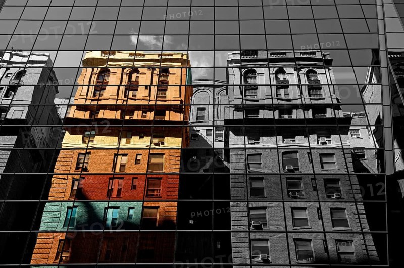 Houses are reflected in the glass facade of a skyscraper