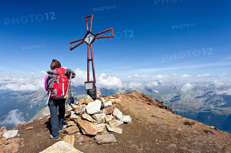 Mountain climber at the summit cross on Schneebiger Nock Mountain in the Rieserferner Group