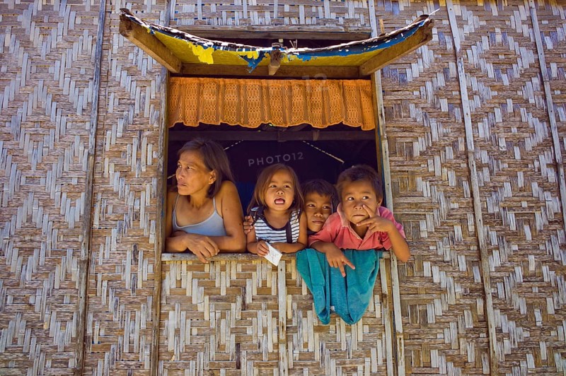 Filipino mother and children looking out of a window of their home