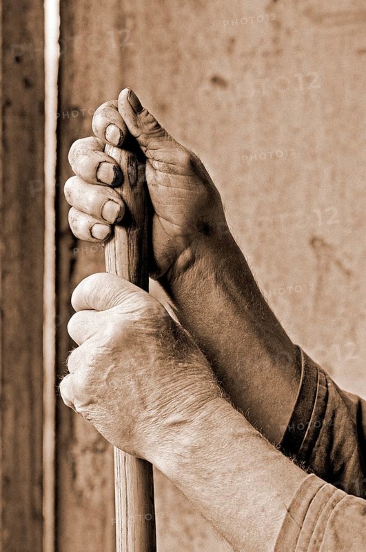Hands marked by hard work supported on a pitchfork