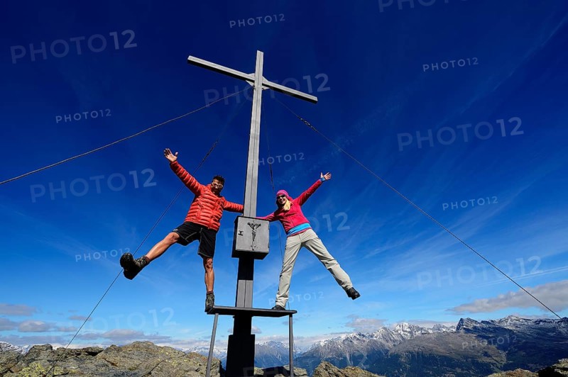 Hikers on the summit cross on the summit of Boeses Weibele Mountain in the Defregger Group