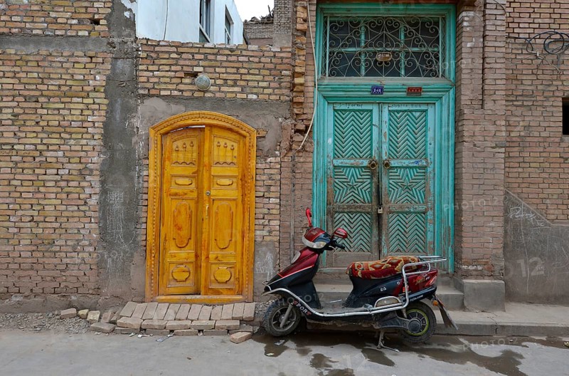 Motor scooter in front of old Uighur Muslim doorframes in new homes