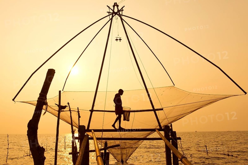 Fisherman holding a landing net in a Chinese fishing net at sunrise