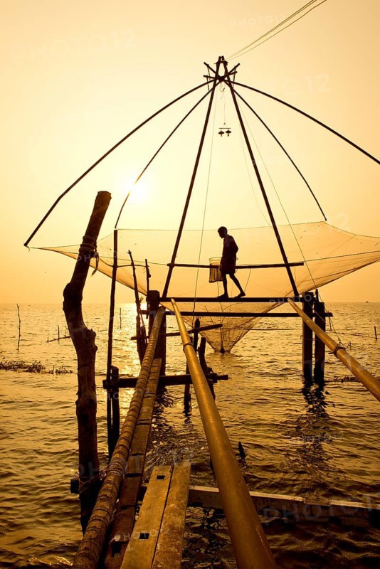 Fisherman holding a landing net in a Chinese fishing net at sunrise