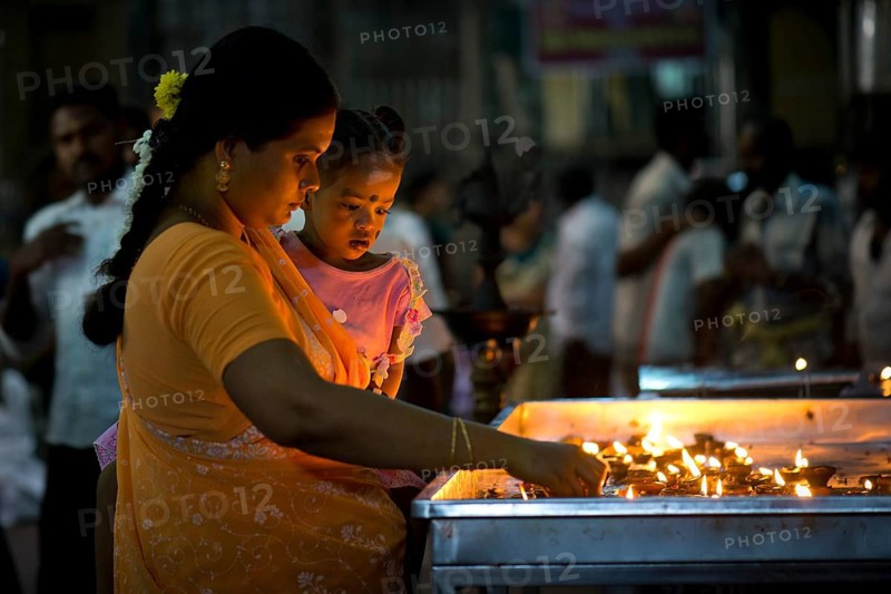 Woman holding a child in her arms while lighting oil lamps in a temple