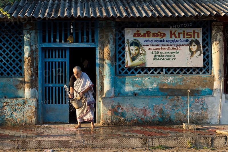 Old woman moistening the pavement in front of her house