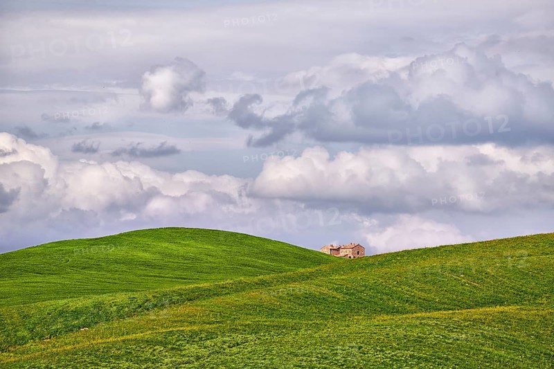Single house between clouds and hilly fields