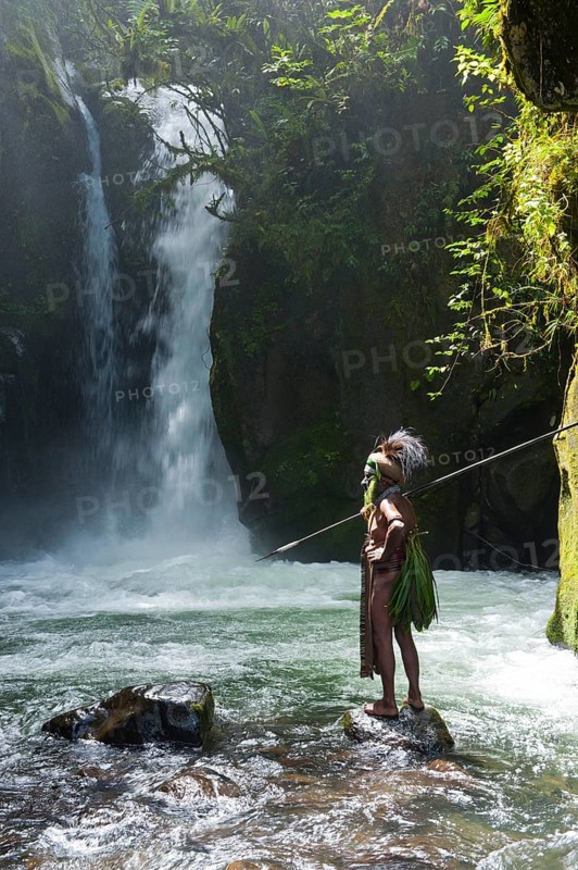 Decorated and painted tribal chief standing in front of a waterfall in the Highlands