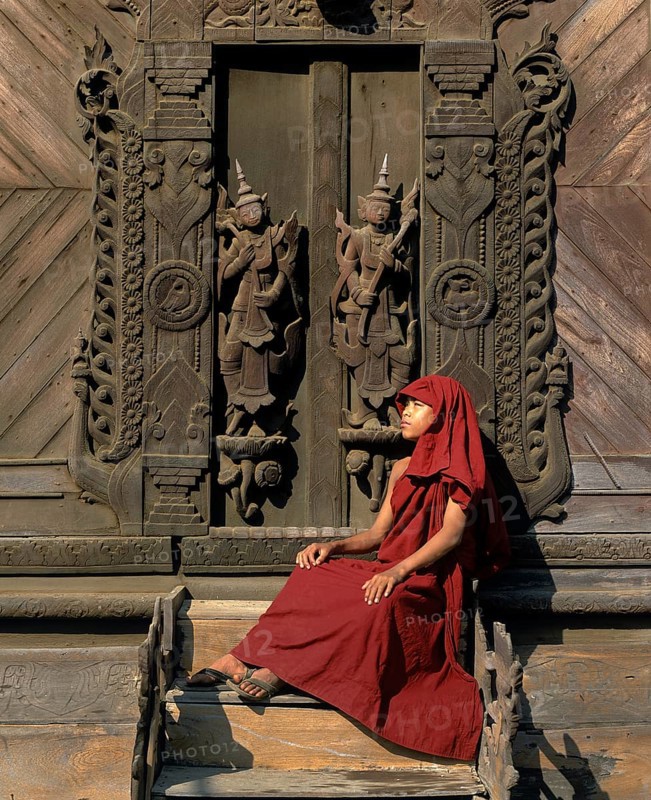 Monk sitting in front of a carved teak door