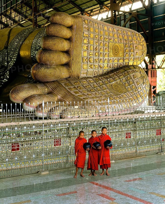 Monks holding begging bowls standing in front of the feet of the Reclining Buddha of Chauk Htat Gyi