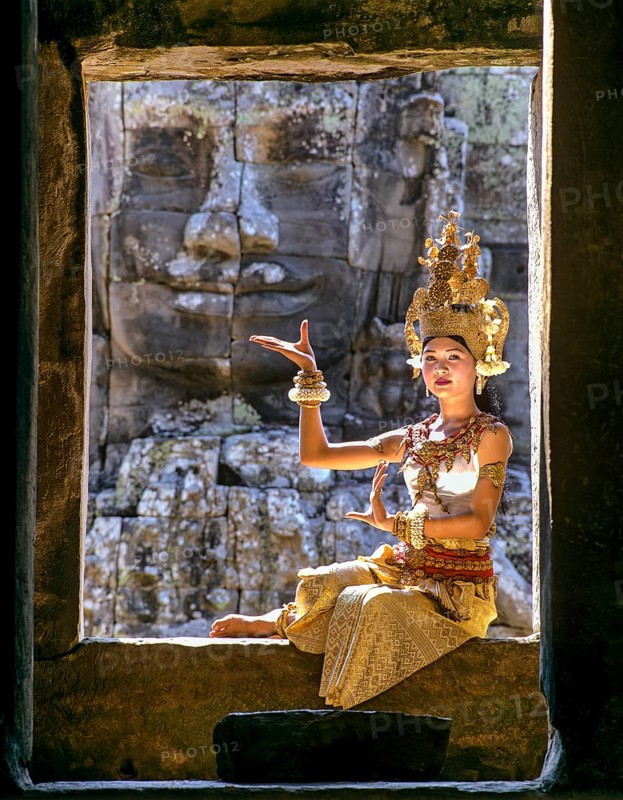 Temple dancer or apsara sitting in a window in front of a face tower at Bayon Temple