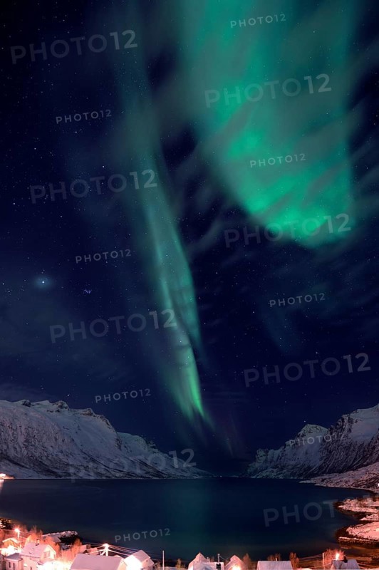 Aurora over a fjord with snow-covered mountains and an illuminated village