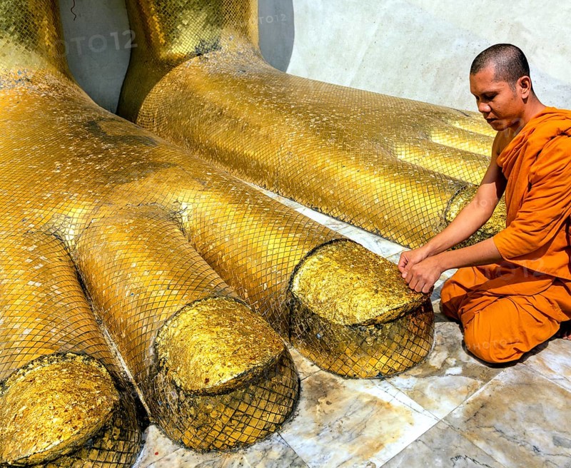 Monk praying at the feet of the golden Buddha statue of Wat Intharawihan