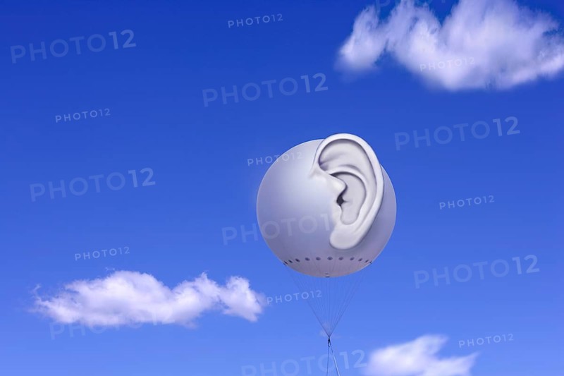 Tethered balloon with a three-dimensional human ear against a blue sky with white clouds