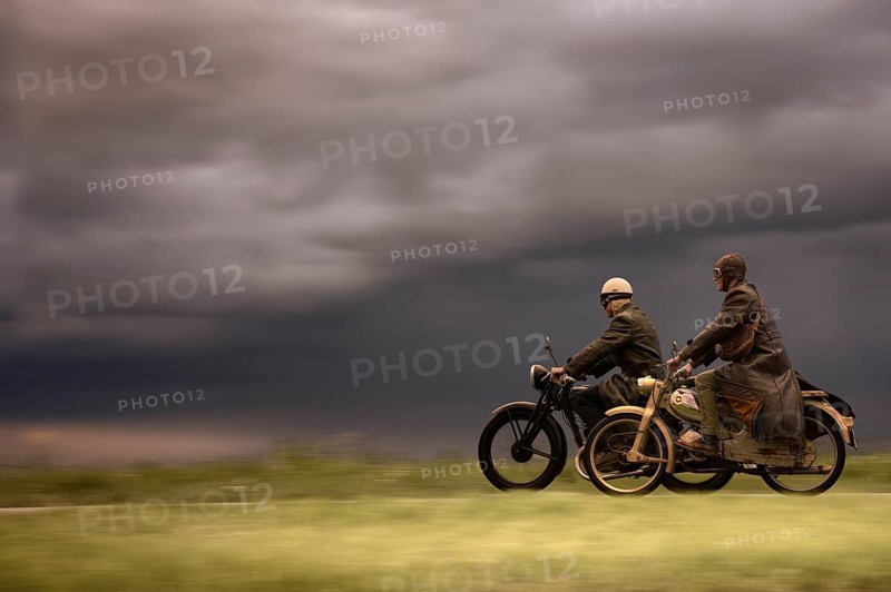 Two vintage motorcyclists in front of a dramatic cloudy sky