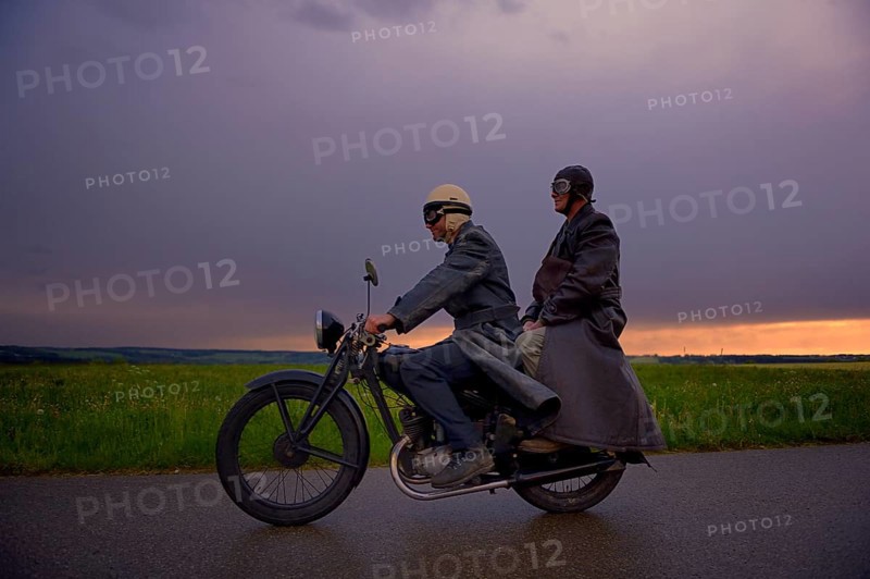 Two vintage motorcyclists in front of a dramatic cloudy sky