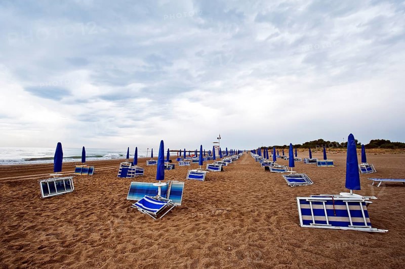 Folded deck chairs and parasols on a beach by the sea with rain clouds