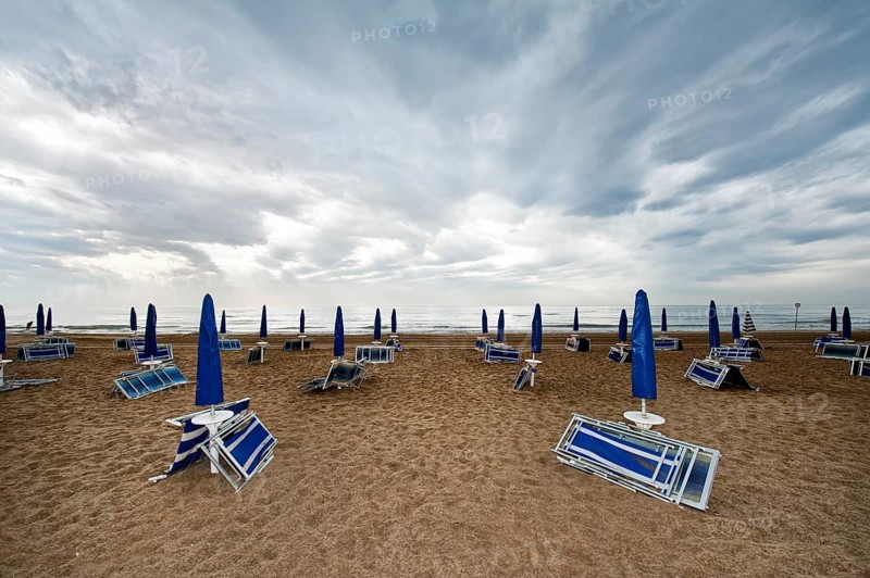 Folded deck chairs and parasols on a beach by the sea with rain clouds