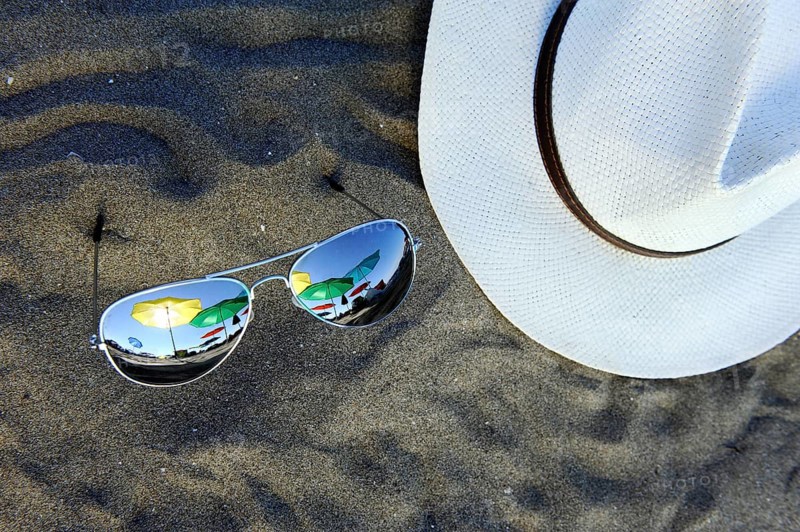 Parasols are reflected in sunglasses lying in the sand