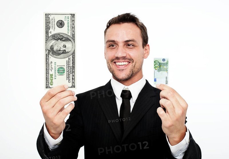 Smiling young man wearing a suit holding a large 100 dollar bill and a small 100 euro banknote