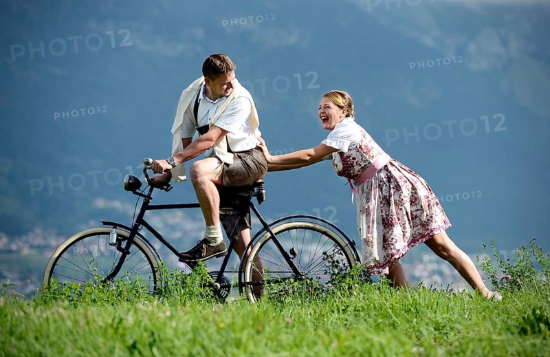 Man and a woman wearing traditional costume with an old bicycle within a natural landscape