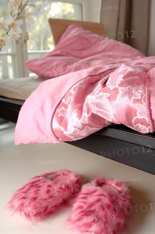 Pink plush slippers are lying next to a bed