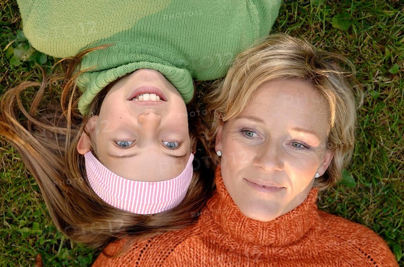 Mother and daughter lying head to head on the grass