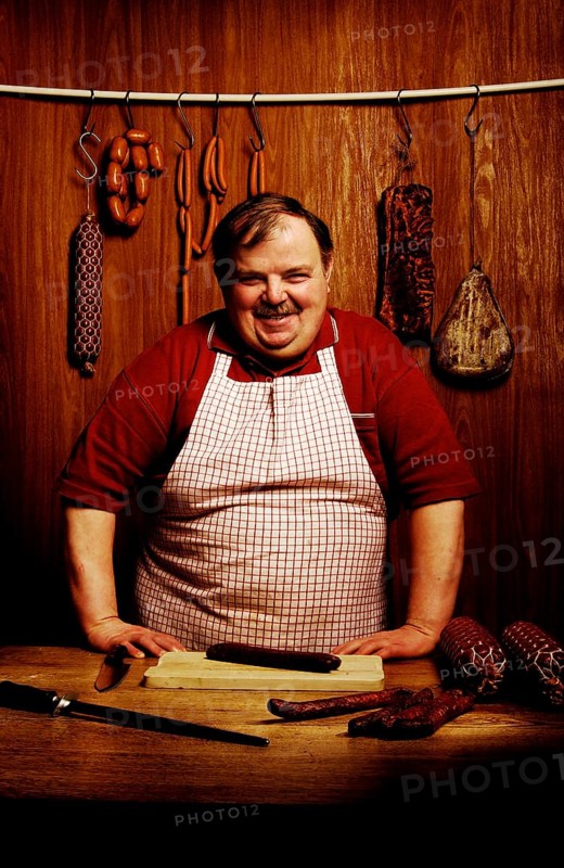 Fat butcher smiling with his hands propped on a bench in a butcher's store with a wooden ambience