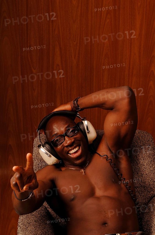Young muscular bare-chested man sitting in an armchair with headphones