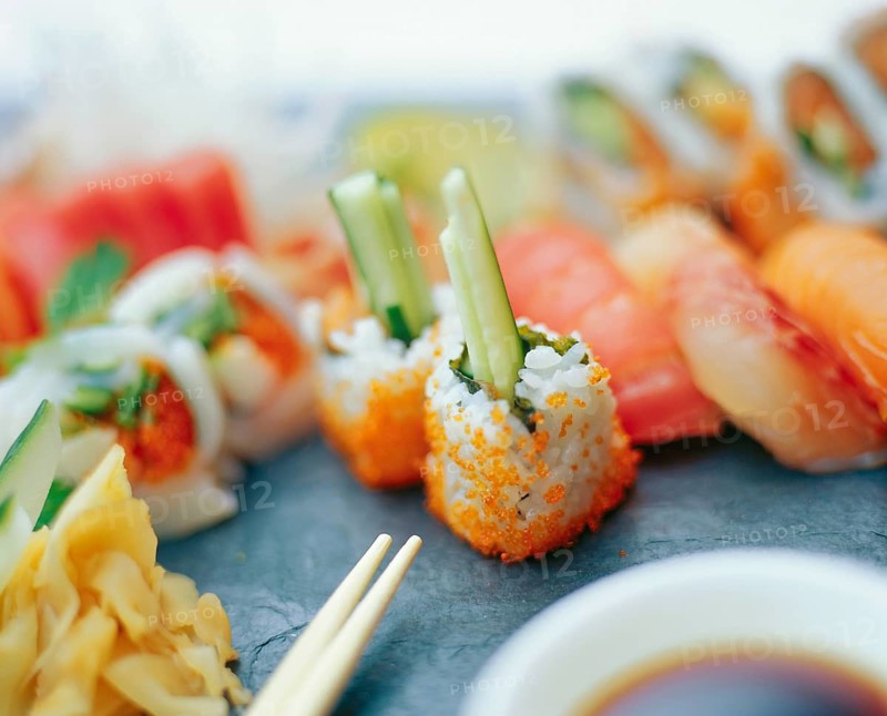 Assorted sushi rolls with pickled ginger and chopsticks on a slate surface