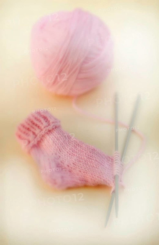 Semi-finished knitted pink baby sock with a ball of wool and knitting needles