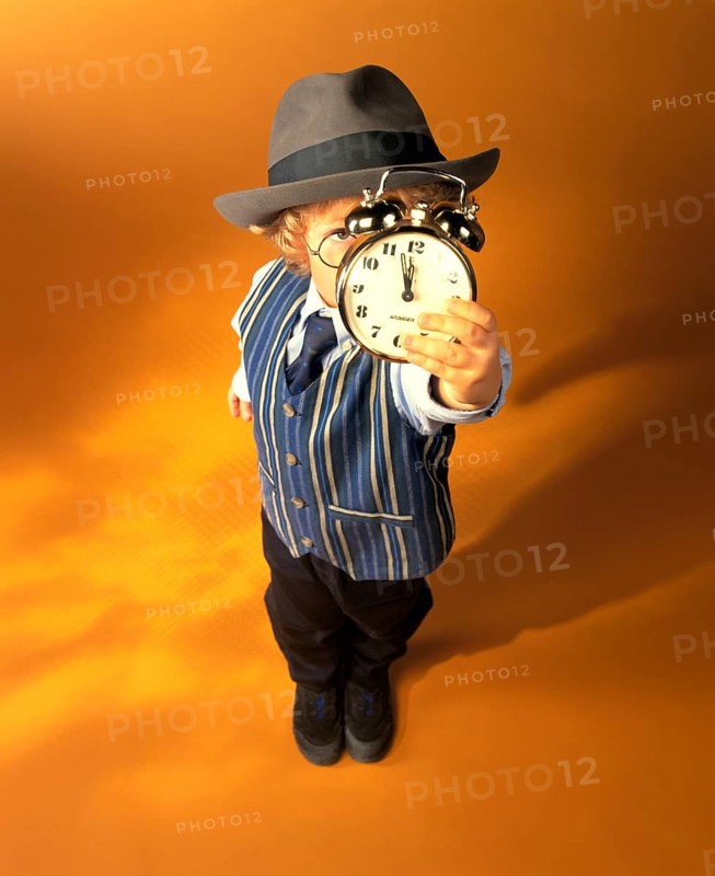 Boy wearing business clothes holding an alarm clock showing eleven fifty-five