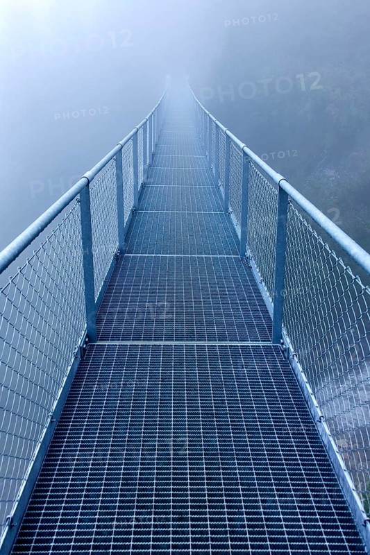 Steel bridge in the fog crossing over an Alpine stream