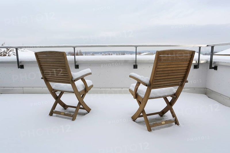 Two snow-covered chairs on a terrace