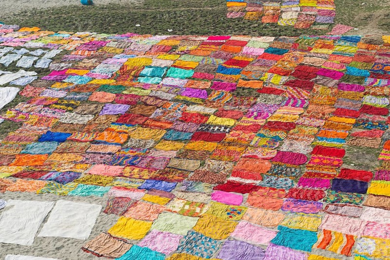 Colourful saris laying to dry after washing on a sandbank on the banks of the Yamuna River