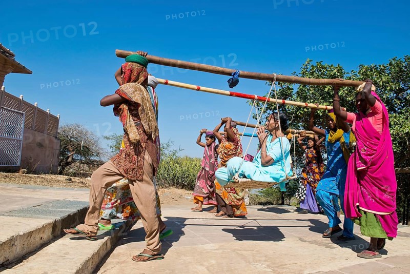 Young Indian women wearing traditional saris carrying long bamboo poles on their heads with a seat for pilgrims climbing the steps to the temple complex