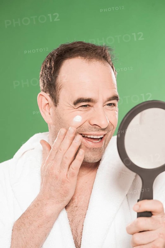 Man wearing a bathrobe looking at himself in a hand mirror