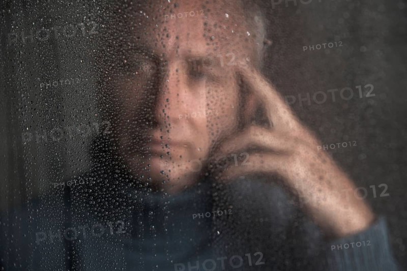 Lonely man sitting behind a window covered in rain drops
