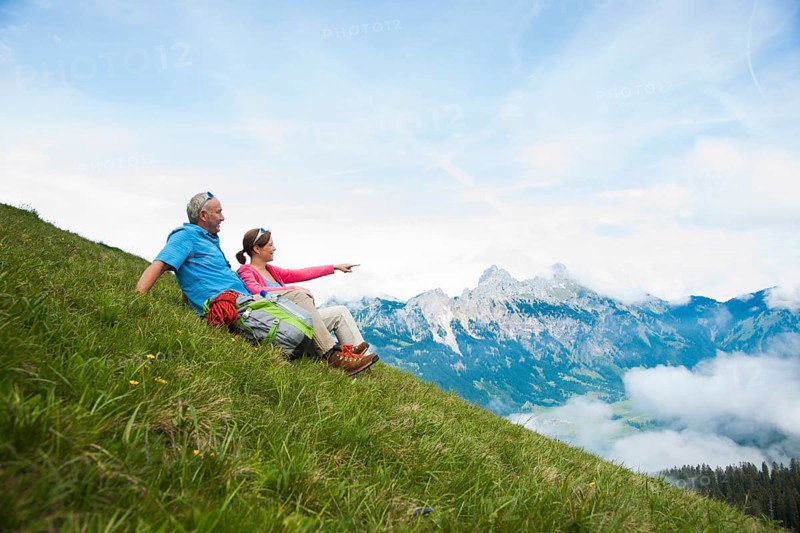 Hikers sitting on a mountain meadow and enjoying the view of the Tannheim mountains