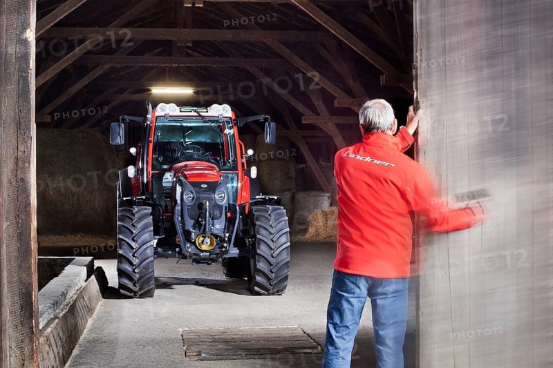 Farmer opening a barn door revealing a tractor behind it