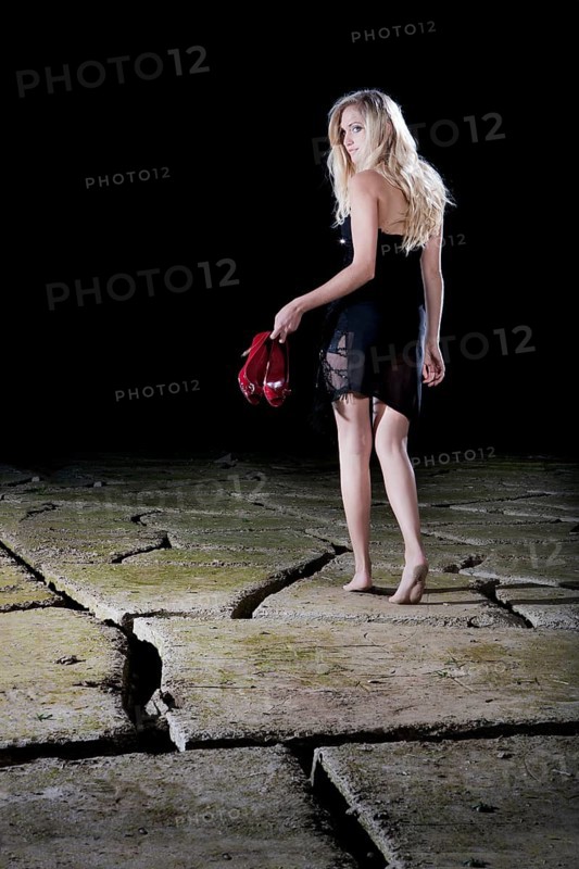 Young woman walking barefoot in an evening dress across cracked clay
