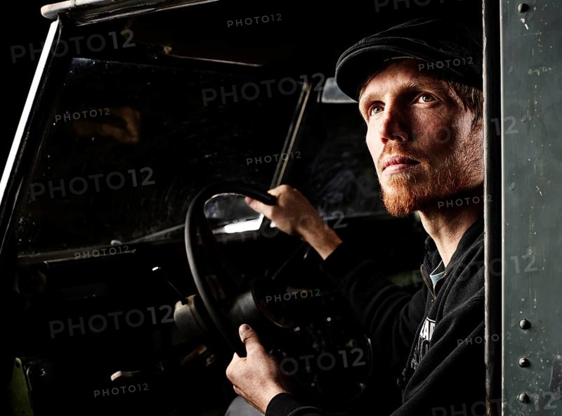 Man with a hat sitting in the driver's seat of an old car