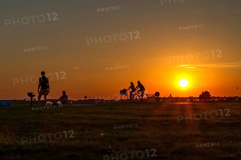 Couple having a barbecue on Tempelhof Airfield in the evening sun in front of two passing cyclists