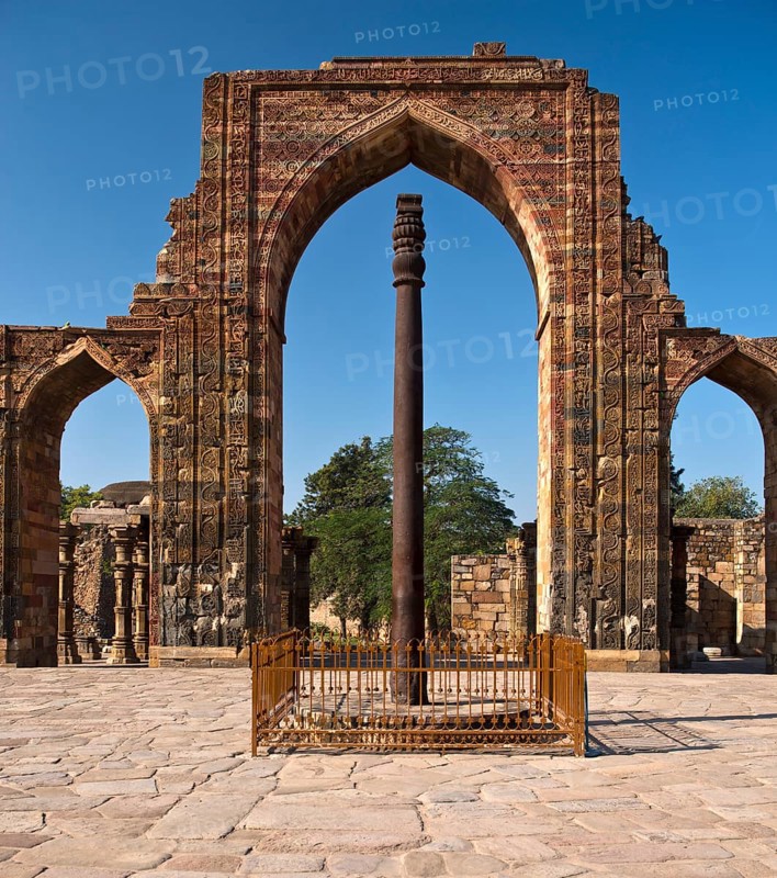 Entrance portal of the Quwwat-ul-Islam Masjid Mosque with relief decorations and an iron pillar in the courtyard