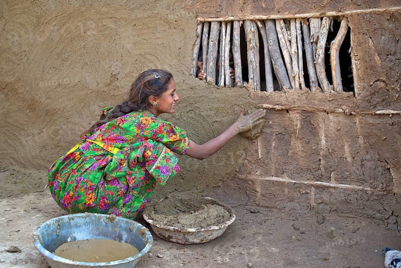 Girl in traditional dress plastering the wall of a house with a mixture of water