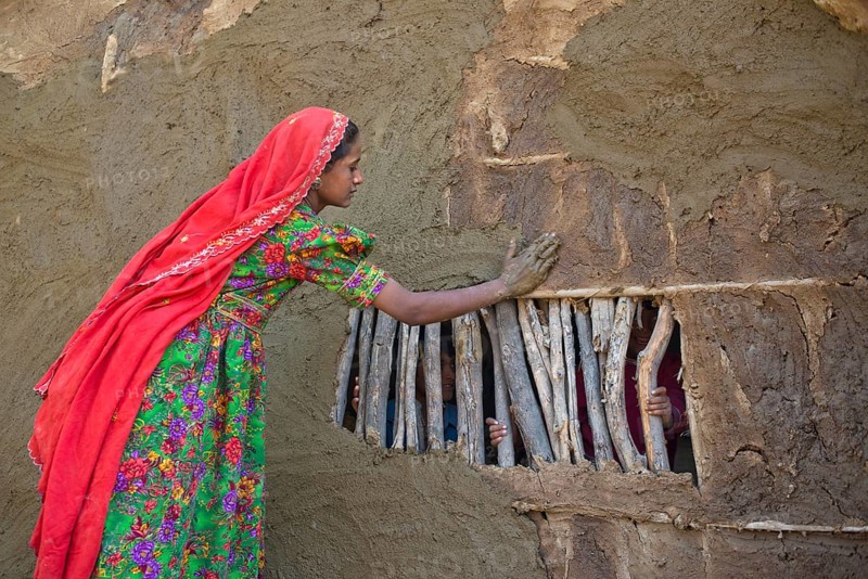 Girl in traditional dress plastering the wall of a house with a mixture of water