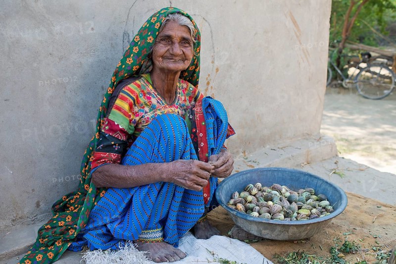 A friendly elderly woman in traditional dress sitting on the ground sorting small melons