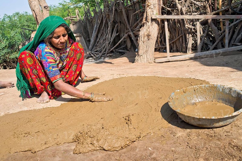 Woman in traditional dress plastering the floor of a courtyard with a mixture of water