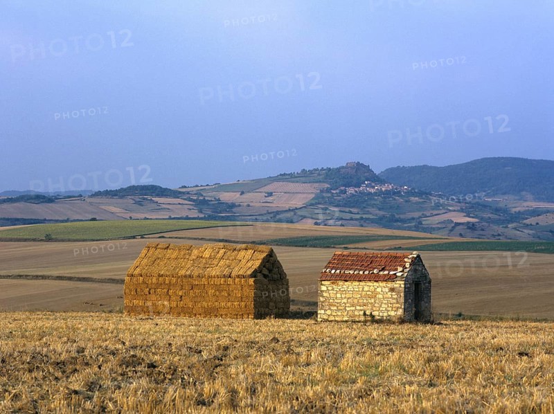 Bales of straw stacked in the shape of a house next to a little stone house
