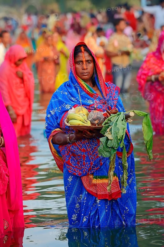 Woman wearing a blue sari with offerings standing in water during the Hindu Chhath Festival